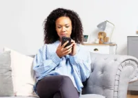 Smiling woman in her living room reviewing an ECO4 grant proposal on a phone.