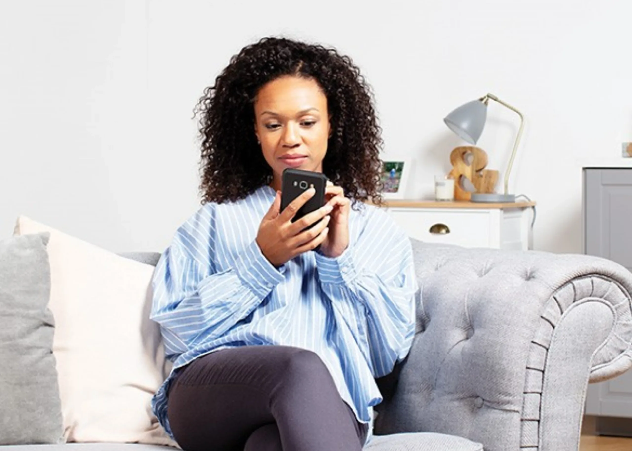 Smiling woman in her living room reviewing an ECO4 grant proposal on a phone.