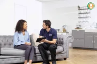 Energy advisor in company uniform discussing documents with homeowner on living room sofa, showing tablet with ECO4 eligibility checklist